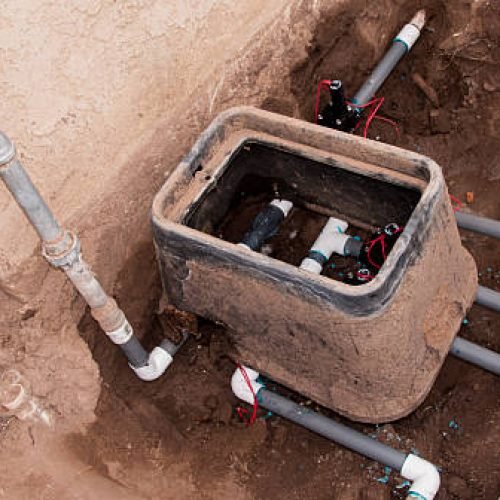 This view shows PVC piping, valves, connectors, and wiring for an underground sprinkler system for a residential lawn.